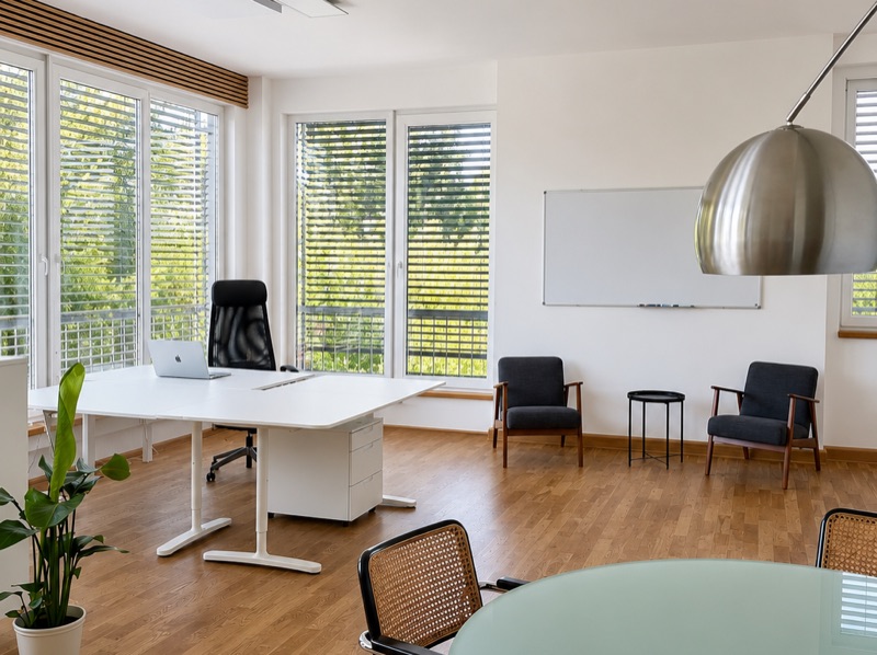 Schreibtisch am Fenster, daneben zwei Sessel und ein Whiteboard
