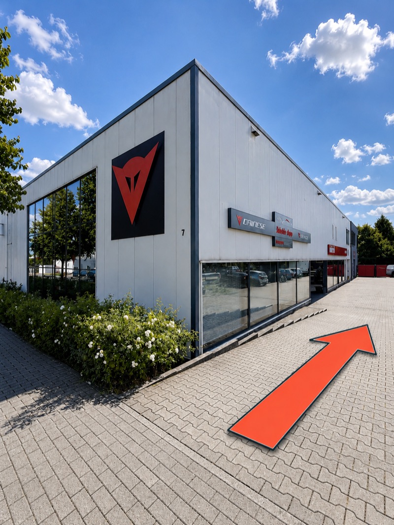 Das Gebäude vom Parkplatz aus, an der Ecke die Hausnummer 7; ein oranger Pfeil zeigt den Weg an der Glasfront entlang bis zum Eingang